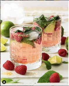 two glasses filled with raspberry mojitas and limes on a table