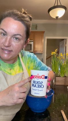 a woman in an apron holding up a bowl of sour cream