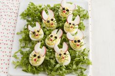 an arrangement of deviled eggs decorated like mice with green lettuce and radishes