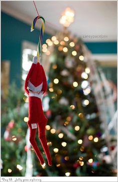 an elf hanging from a string in front of a christmas tree