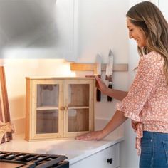 a woman standing in front of a wooden cabinet holding a spatula and looking at it