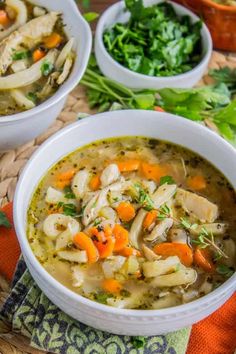 two white bowls filled with chicken noodle soup on top of a woven place mat