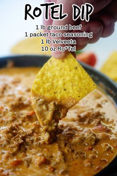 a hand holding a tortilla chip over a bowl of chili and cheese dip