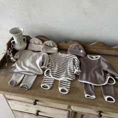 several knitted baby clothes are laid out on a wooden dresser next to a coffee cup