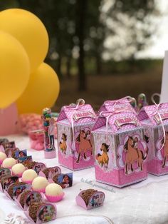 there is a table with pink boxes and decorations on it, along with balloons in the background