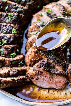 a plate with steaks and sauce being drizzled on it by a spoon