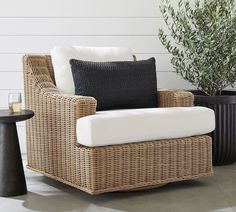 a wicker chair with black and white pillows next to a small potted plant