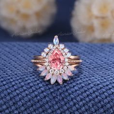 an image of a ring with pink and white stones on it sitting on a blue cloth