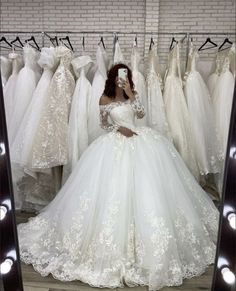 a woman taking a selfie in front of wedding gowns on display at a store