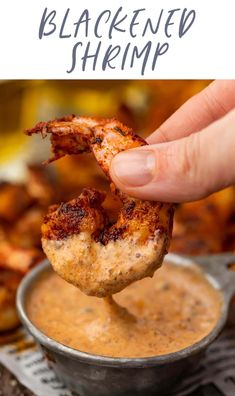 a hand holding up a piece of grilled shrimp over a bowl of dipping sauce