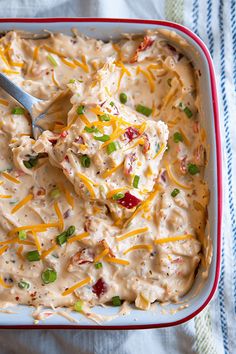 a red and white casserole dish filled with cheese, green onions, and other toppings