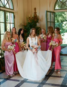 a group of women standing next to each other in front of a window holding bouquets