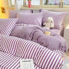 a bed with purple and white striped comforter next to a stuffed animal on top of it