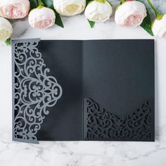 two black cards with intricate laser cut designs on them and roses in the back ground