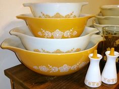 a stack of yellow and white dishes sitting on top of a wooden table next to vases