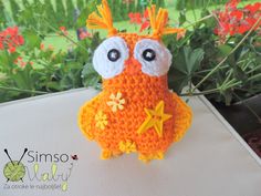 an orange crocheted owl sitting on top of a table next to some flowers