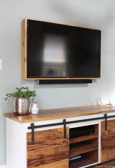 a flat screen tv mounted on the wall above a wooden entertainment center with sliding doors