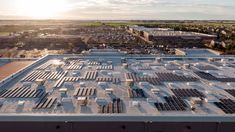 an aerial view of solar panels on the roof of a large building with buildings in the background