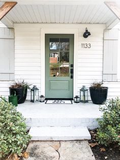 the front door of a white house with three planters