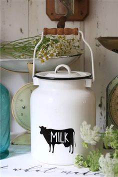 a white milk can with a black cow sticker on the side and flowers next to it