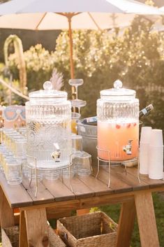 an outdoor picnic table with drinks and ice buckets on it, surrounded by wicker baskets