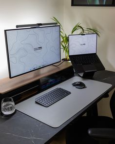 two laptops sitting on top of a desk next to a keyboard and mouse with a plant in the background