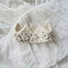 a crocheted crown laying on top of a white bed with ruffled bedspread