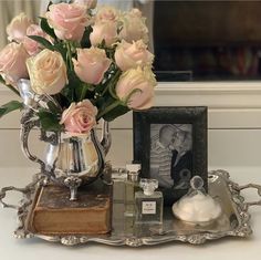 a silver vase with pink roses and an old book on a tray next to it