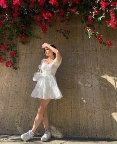 a woman in a white dress standing next to a wall with red flowers on it