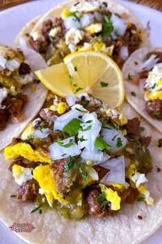 three tacos on a plate with lemon wedges