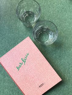 two empty glasses sitting on top of a table next to a pink book with green writing