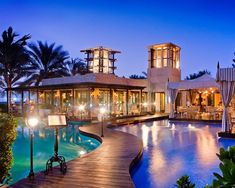 an outdoor swimming pool surrounded by palm trees at night with lights on the water and large clock tower in the background