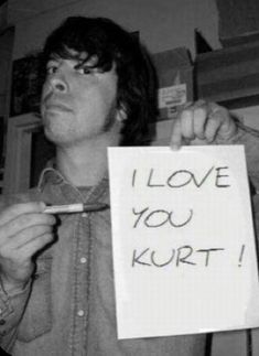 a man holding a sign that says i love you kurt in black and white