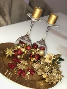 two wine glasses sitting on top of a gold platter with christmas decorations around them