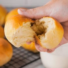 a person holding a piece of bread in their hand next to some rolls on a cooling rack