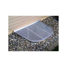 a metal grate sitting on the side of a house next to gravel and rocks