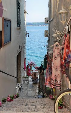 an alley way leading to the ocean with clothes hanging on racks and flowers in pots