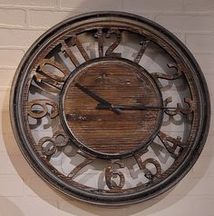 a large wooden clock mounted to the side of a brick wall with numbers on it