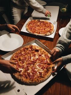 two pizzas are being cut and served in boxes on a table with people around them