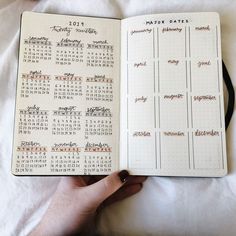 a hand holding an open planner book on top of a white sheet with writing in it