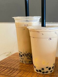 two iced drinks sitting on top of a wooden table with straws in each cup