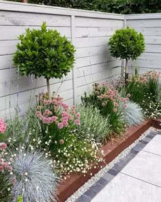 a garden filled with lots of plants next to a white fence and stone flooring