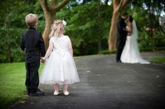 a young boy and girl dressed in formal wear standing on a path with trees behind them