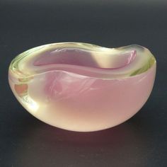 a pink and green glass bowl sitting on top of a black table next to a white wall