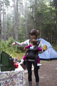 a woman holding a child in her back while camping