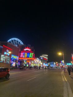 people are walking down the street in front of an amusement park and rides at night