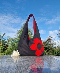 a black bag with red flowers on it sitting on top of a stone table in front of some bushes