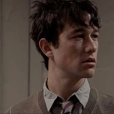 a young man wearing a vest and tie looking off to the side with serious expression on his face