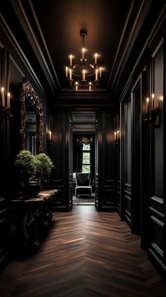 an empty hallway with dark walls and wood flooring is lit by candle lights from the chandelier