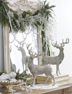 two silver deer statues sitting on top of a table next to a mirror and christmas decorations